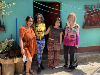 4 colorfully dressed women posing in front of a turquoise house
