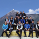 About 20 nicely dressed teenage kids sitting on a stair pyramid posing for a photo with a volcano in the background