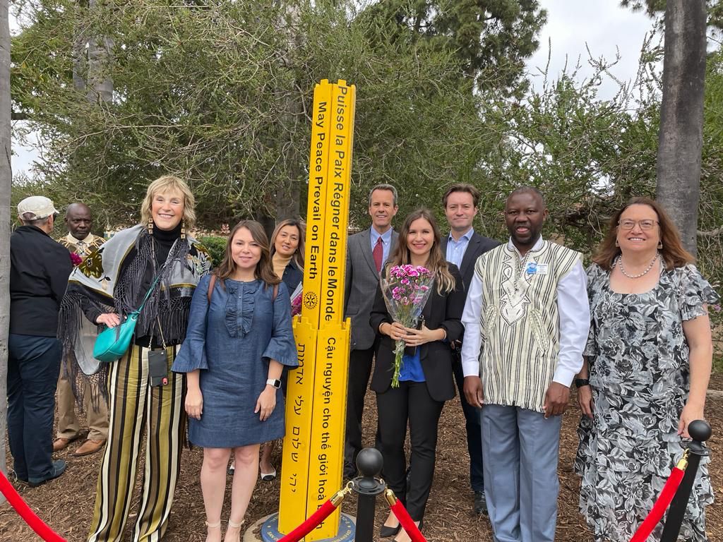 group of people standing next to yellow peace pole for group photo